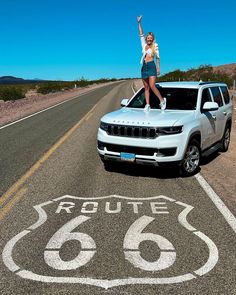 a woman standing on the hood of a white jeep in front of a route 66 sign