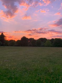 the sky is pink and purple as the sun sets over a grassy field with trees in the background