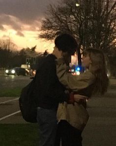 two people standing next to each other on a street at night with traffic lights in the background