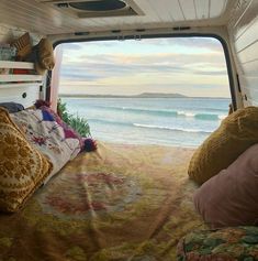 the inside of a camper with a bed and pillows on it, looking out at the ocean