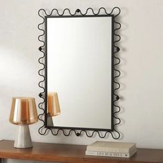 a mirror sitting on top of a wooden table next to a lamp and a book