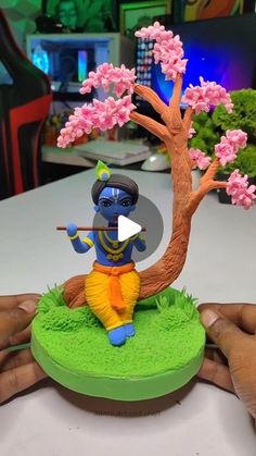 someone is holding a small figurine in front of a tree with pink flowers