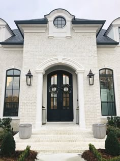 a white brick house with black doors and two large planters on the front steps