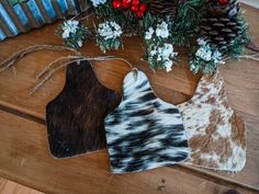 two cow hide ornaments sitting on top of a wooden table next to pine cones and berries