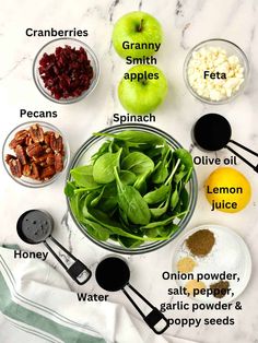 the ingredients for an apple smoothie laid out on a marble counter top, including spinach, almonds, cranberries, pecans, and apples