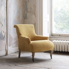 a yellow chair sitting in front of a window next to a radiator on a wooden floor