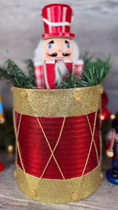 a red and gold tin can with a small christmas decoration in the center on a wooden table