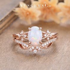 a white opal and diamond ring sitting on top of a wooden table next to flowers