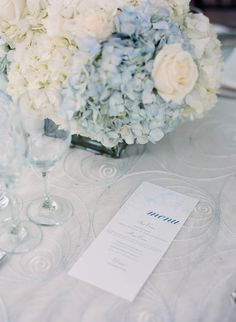 the table is set with white and blue flowers, wine glasses, and menu cards