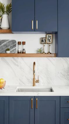 a kitchen with blue cabinets and marble counter tops, gold faucet, brass accents