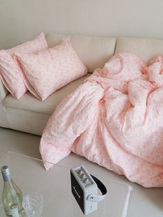 a white couch with pink sheets and pillows on it next to a bottle of wine