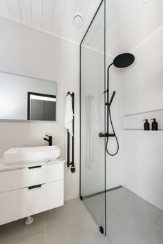 a white bathroom with a glass shower door and black faucet, sink and mirror