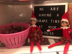 two elfs are sitting next to a bowl of grapes and a sign that says we are having a grape time at your house