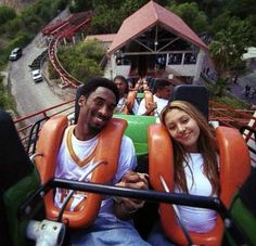 two people sitting on a roller coaster at an amusement park, smiling for the camera