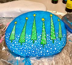 a painted rock sitting on top of tin foil covered in frosting and christmas trees