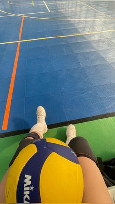 a person sitting on the ground with their feet up in front of an indoor basketball court