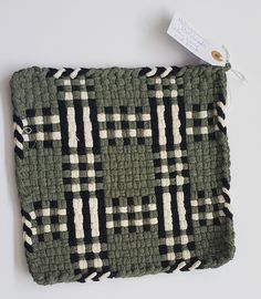 a green and white checkered knitted cushion with a tag on the top of it