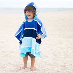 a little boy standing on top of a sandy beach covered in a blue and white towel