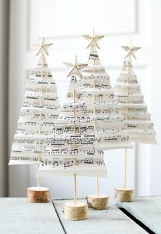 three christmas trees made out of sheet music are sitting on top of a wooden table