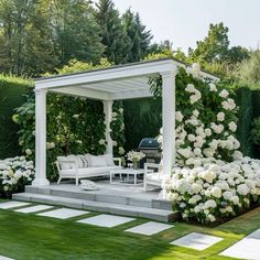 an outdoor living area with white flowers and greenery on either side of the gazebo