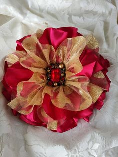 a red and gold flower brooch sitting on top of a white lace table cloth