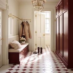 a hallway with white and red tile flooring next to a coat rack filled with coats