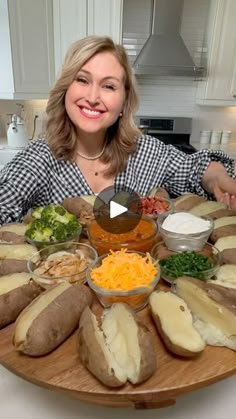 a woman sitting in front of a wooden platter filled with baked potatoes and cheese