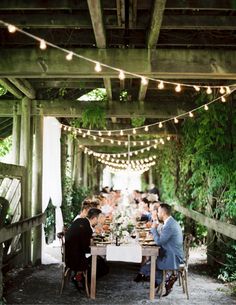 a group of people sitting at a table under an overpass with lights strung from the ceiling