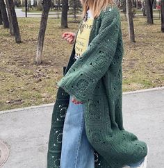 a woman standing on the sidewalk wearing a green cardigan