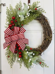 a christmas wreath with red and white bows hanging on the front door, decorated with greenery