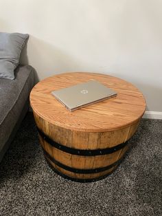 a laptop sitting on top of a wooden barrel table next to a gray couch in a living room