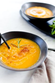 two black bowls filled with soup on top of a white table