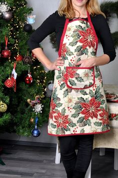 a woman standing in front of a christmas tree wearing an apron with poinsettis on it