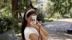 a woman is taking a photo with her cell phone in the park while sitting on a bench