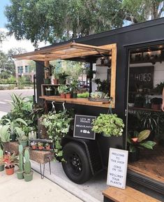 a man standing next to a black truck with plants on it's side and shelves full of potted plants