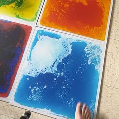 four different colored paintings on the ground with someone's hand in front of them