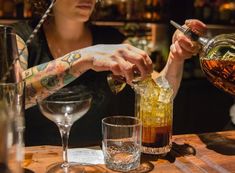 a woman pouring drinks into glasses at a bar with other liquors on the table