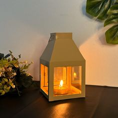 a lit candle sits on a table next to a potted plant