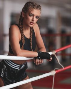 a beautiful young woman standing next to a boxing ring with her hand on the ropes