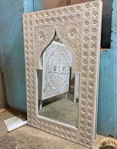 an ornate white mirror sitting on top of a floor next to a blue wall and door