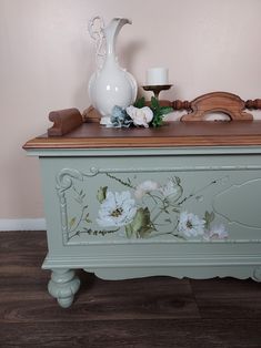 a painted chest with flowers on it and a white vase sitting on top of it