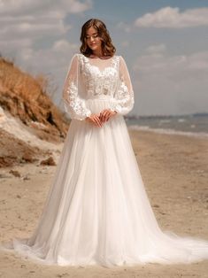 a woman standing on top of a sandy beach wearing a white dress and long sleeves