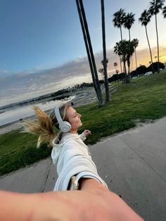 a woman is walking down the sidewalk with her headphones in her hand and palm trees in the background