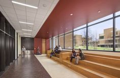 students sit on the steps in an empty hallway with large windows and red painted walls