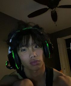 a young man wearing headphones and looking at the camera while standing in front of a ceiling fan