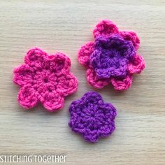 three crocheted flowers sitting on top of a wooden table