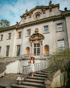 a woman in a white dress is standing on the steps outside an old building with wrought iron railings