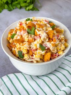 a white bowl filled with corn salad on top of a green and white striped towel