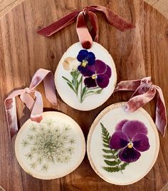 three wooden slices decorated with purple pansies and greenery are on a wood table