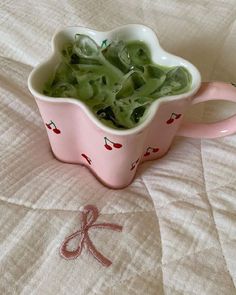 a pink cup filled with green liquid on top of a bed